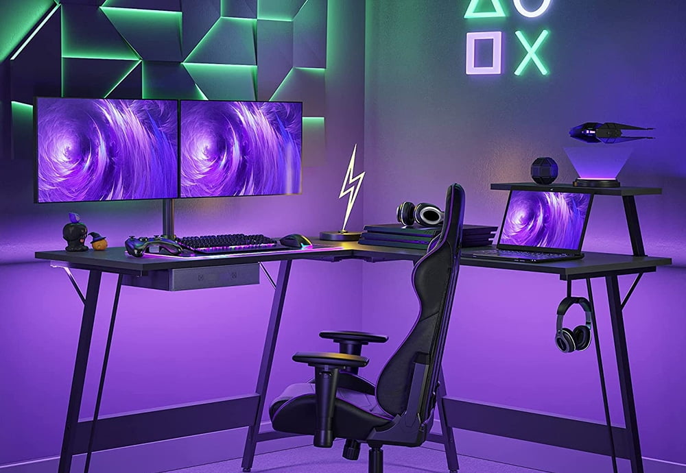 CubiCubi L-shaped gaming desk with drawer, mobile shelf and headset hanger. It has a double monitor and a laprop on it, as well as other accessories and decorative elements.