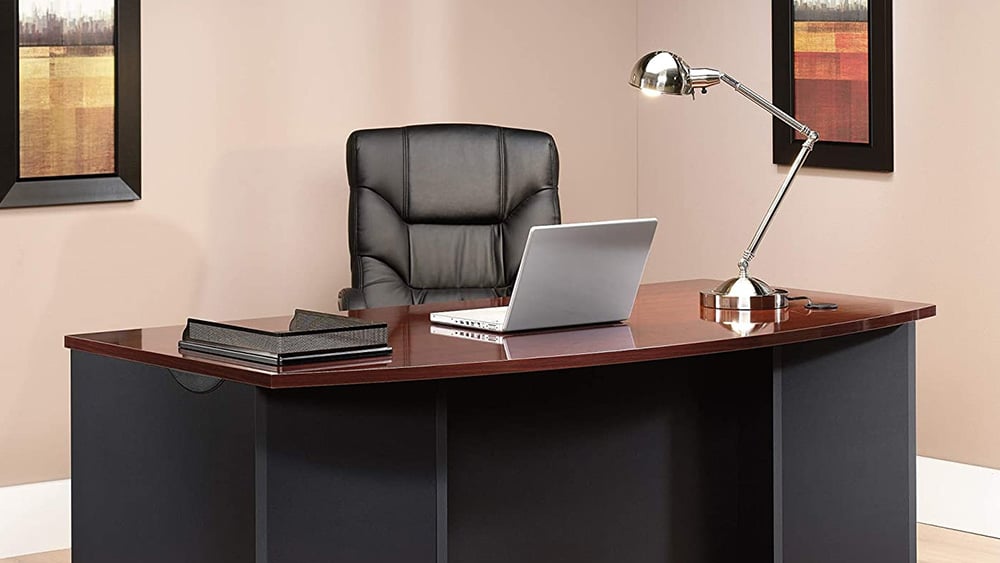 Executive desk with a laptop computer, table lamp and paper tray on it.