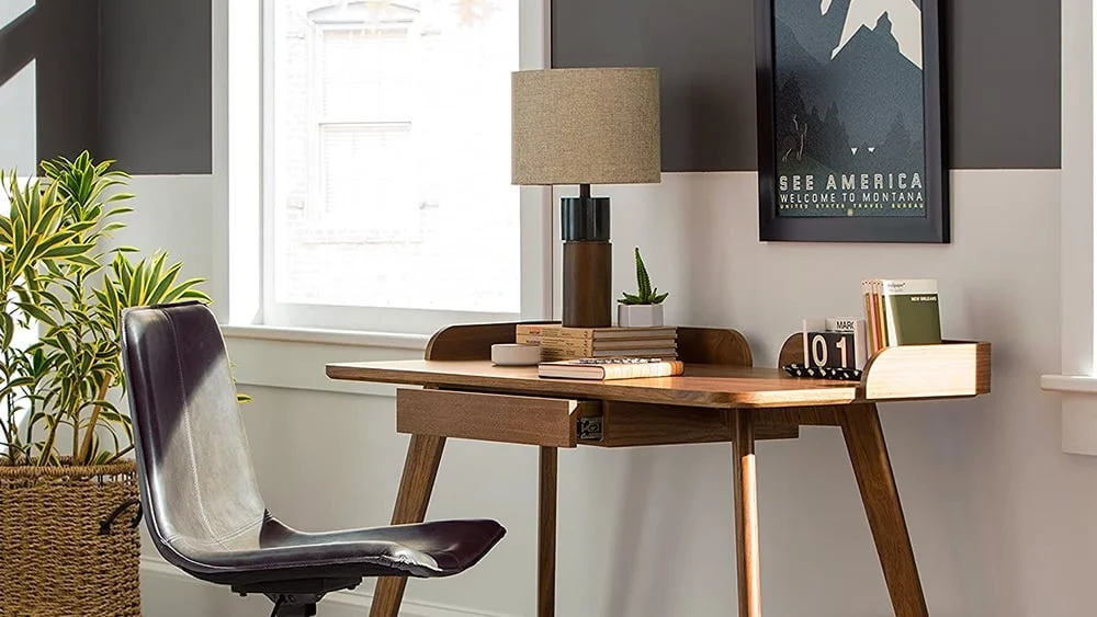 Escritorio de madera maciza, con varios libros y una lampara sobre la mesa